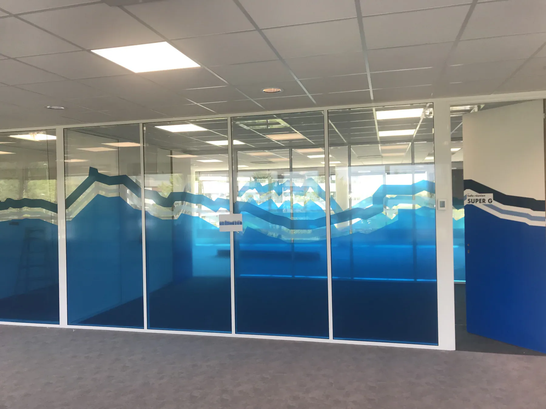 Habillage adhésif bleu à motif montagne posé sur une série de cloisons vitrées de bureaux.