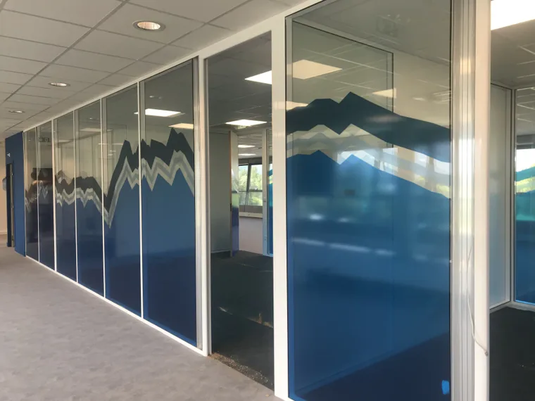 Vue en perspective de cloisons vitrées habillées d’un décor adhésif bleu continu.